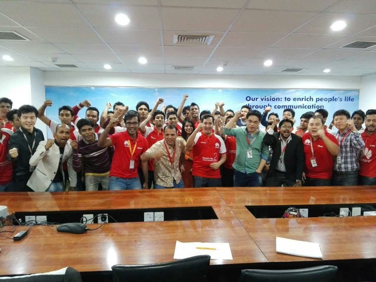 A large Huawei team cheering in a conference room beneath the company vision statement